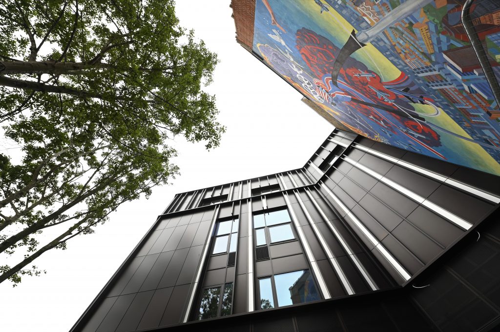 Outside of Brixton House looking up at the outside of the building, with the Nuclear Dawn mural to the right and trees to the left.