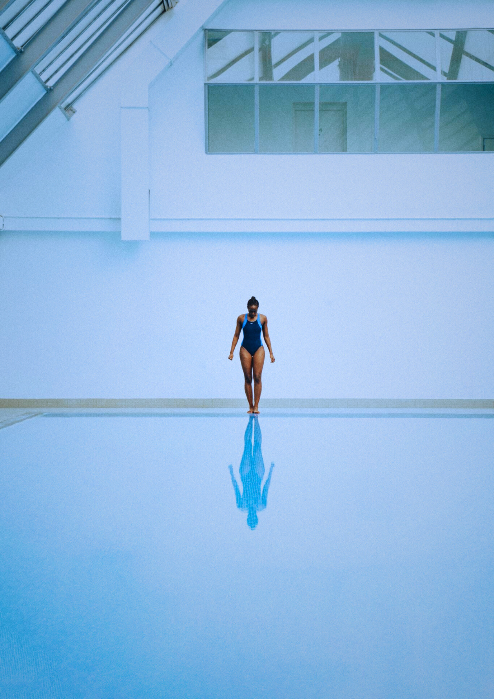 A Black woman looking down at a body of water in a public pool, about to dip her toes in.