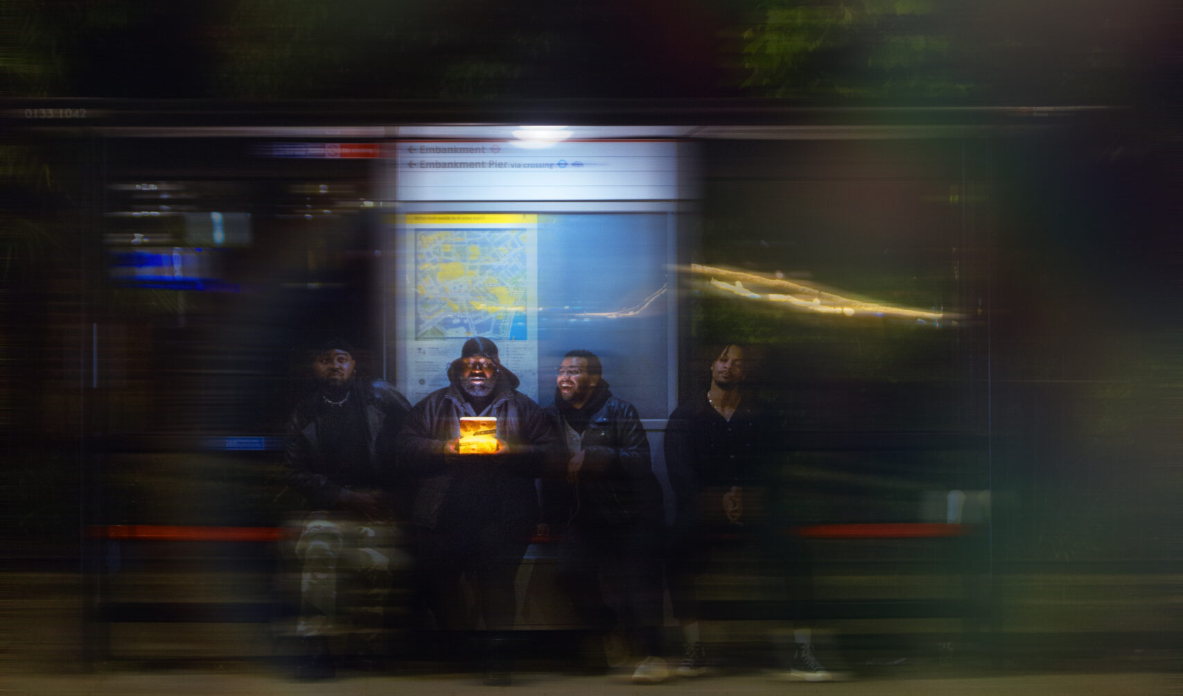 A group of friends on a night out to soho, one can be seen holding a takeaway chicken box. They are waiting at a bus stop.