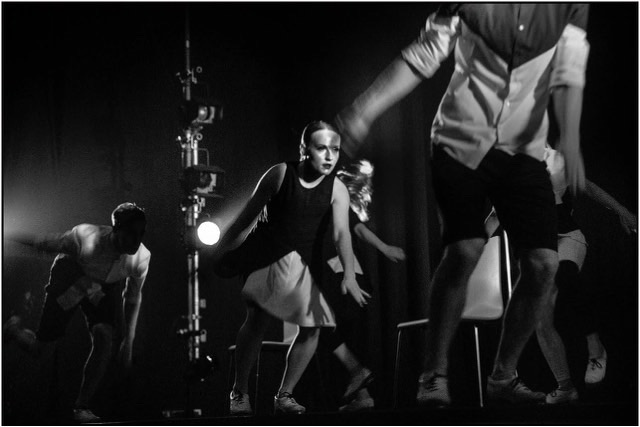 A White woman dancing with an ensemble of dancers, black and white effect